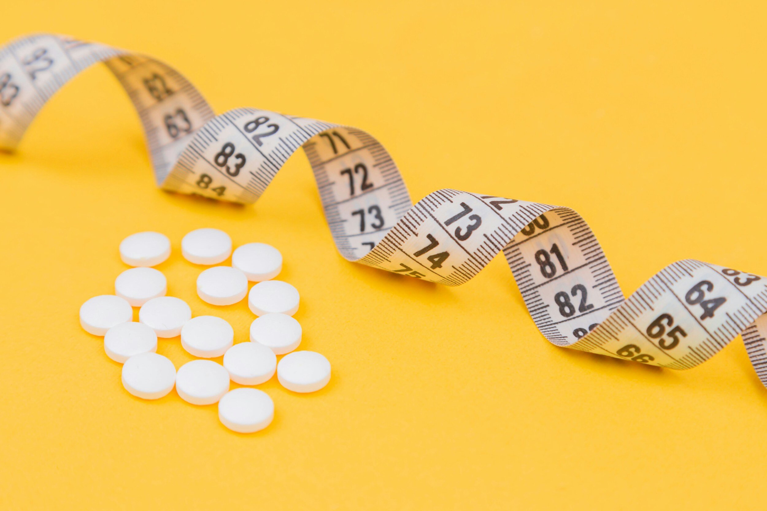 Kranus Health: Pillen neben Maßband auf gelbem Hintergrund