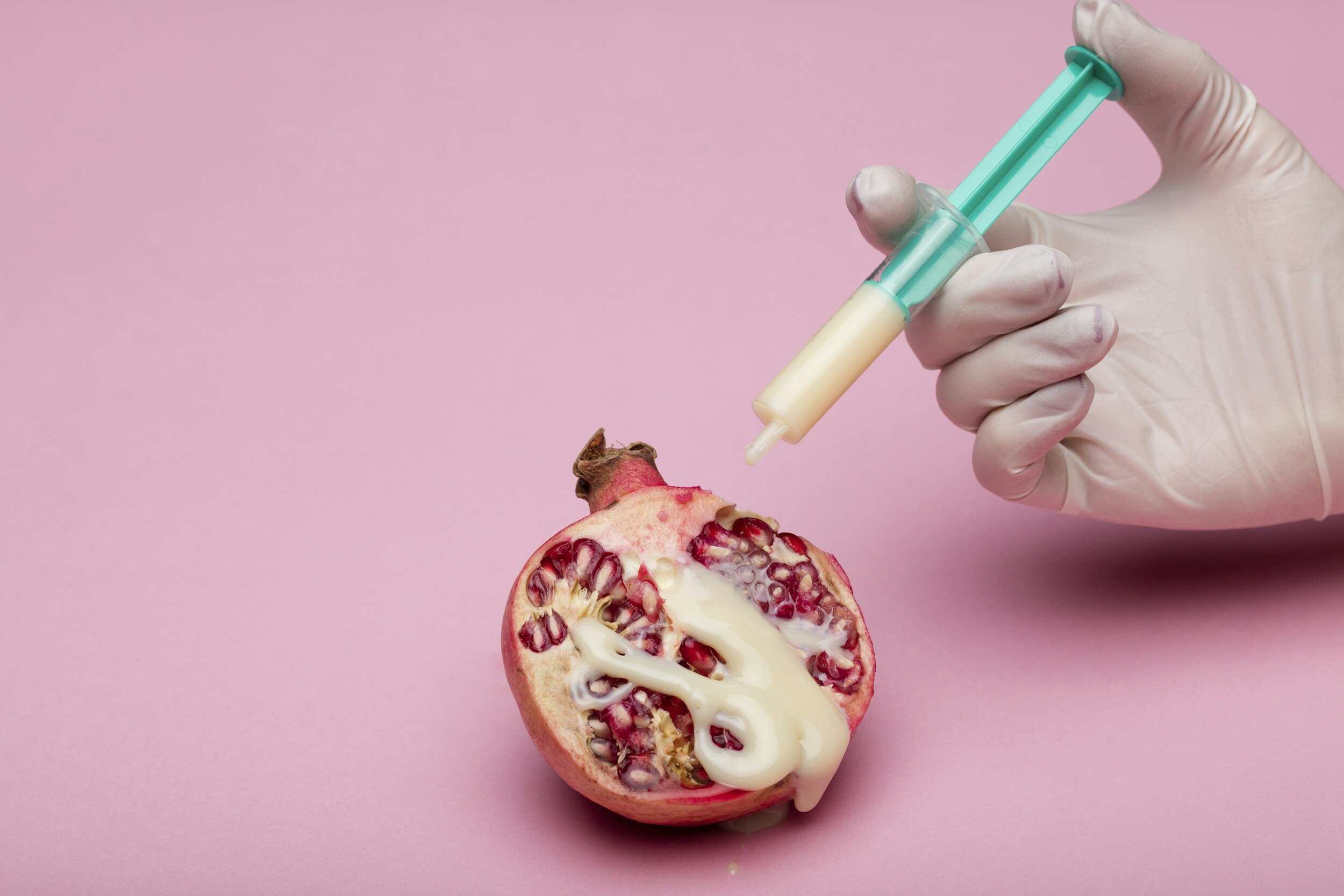 Kranus Health: Granatapfel mit Spritze vor rosa Hintergrund